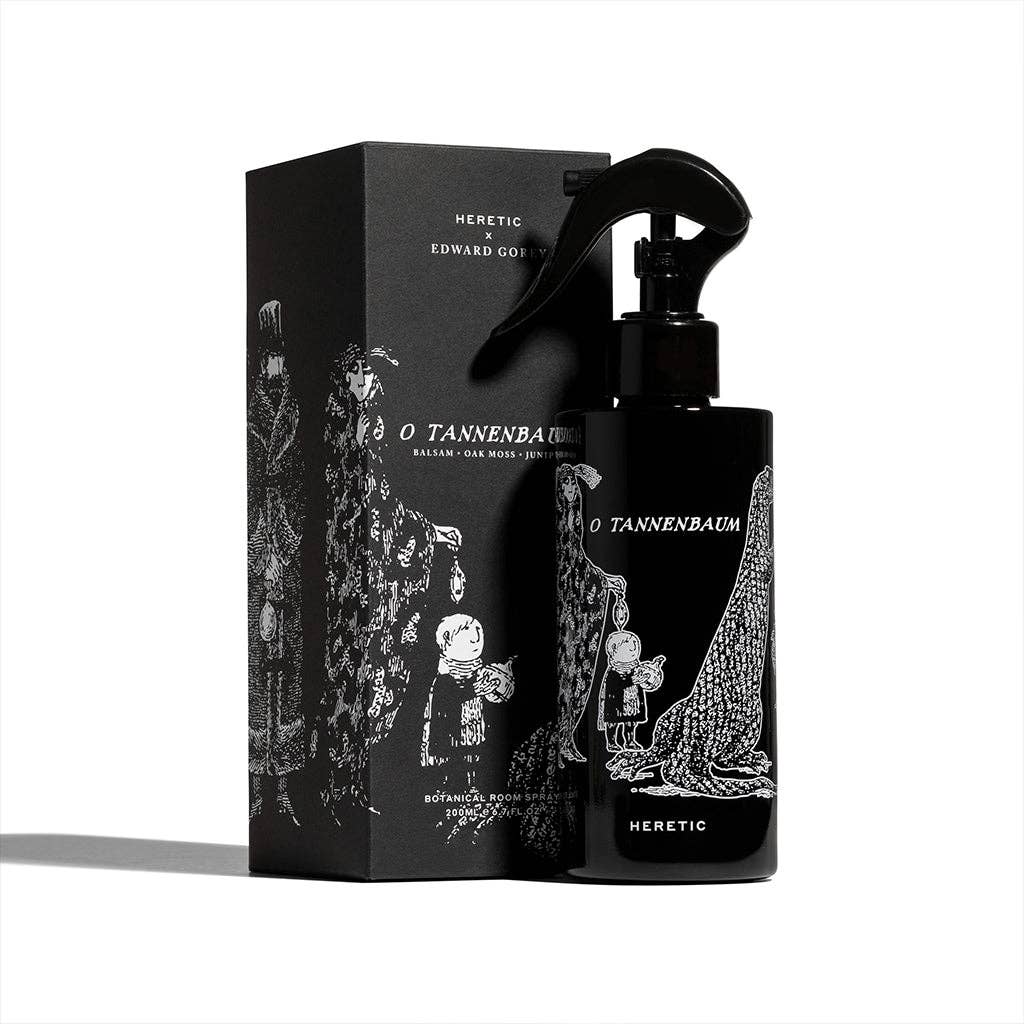 A black O TANNENBAUM ROOM SPRAY: 200ML by Heretic Parfum stands beside its matching box, both adorned with whimsical white figures and a large tree—evoking Edward Gorey's style and perfect for a home fragrance with fir needle notes.