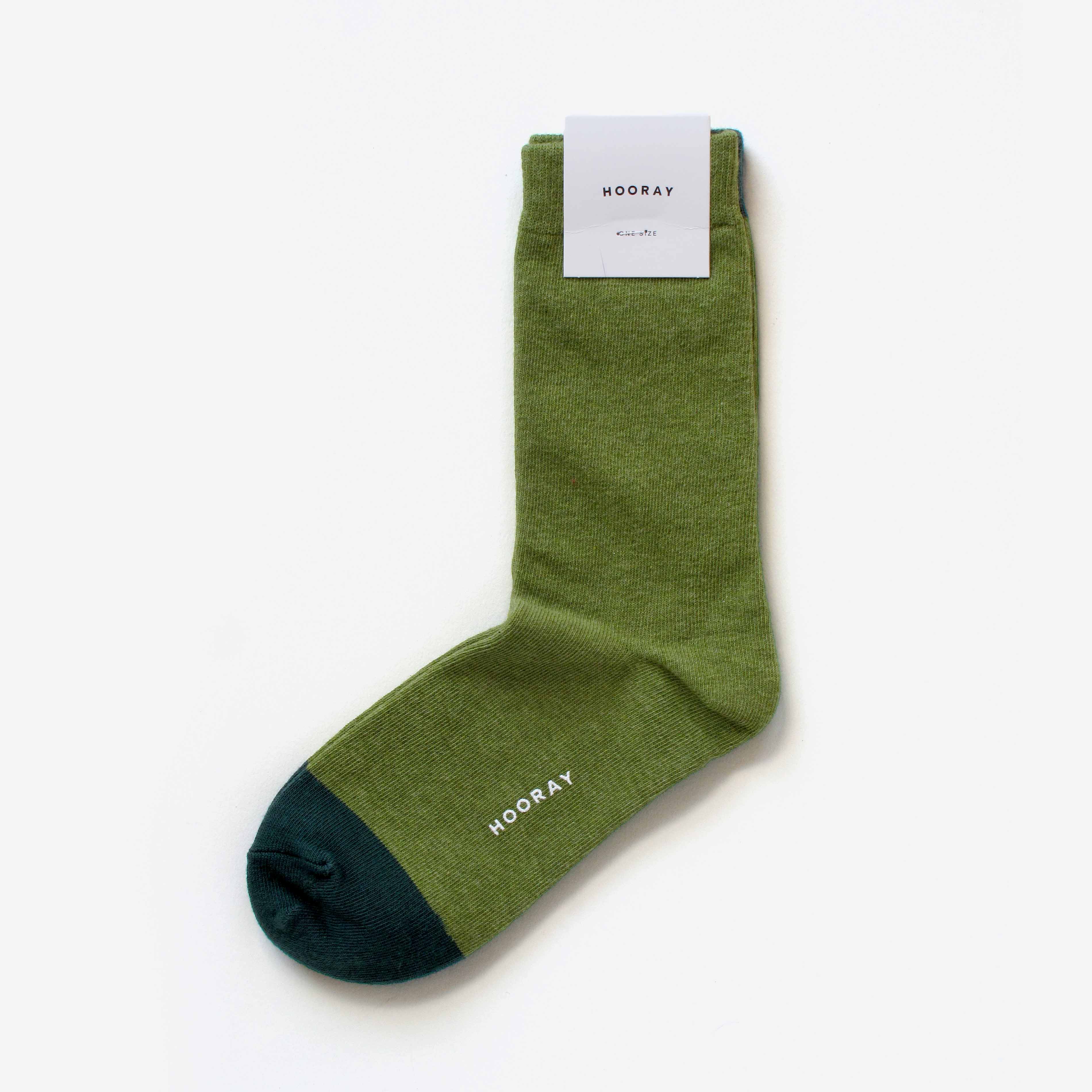 The Lafayette Moss Green Crew Sock by Hooray Sock Co. is a unisex, one-size style in moss green with a dark green toe and “HOORAY” near the toe, shown flat on white with its product label attached at the top.
