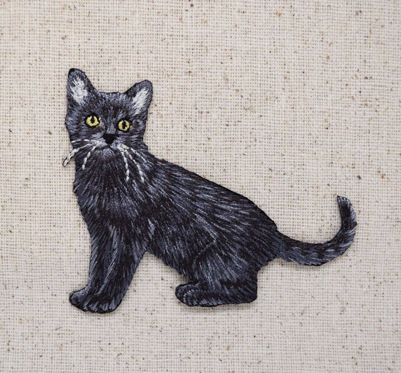 The "Black Cat, Realistic, Full Body" iron on patch by Wholesale Applique features lifelike embroidered details of a kitten with green eyes, making it a striking addition to any patch collection.