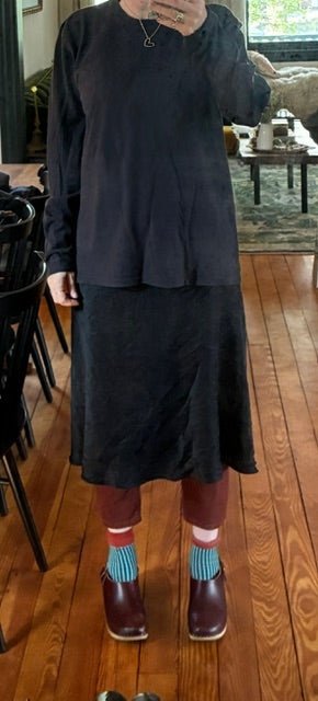 Person wearing a black outfit with brown shoes and blue socks on a wooden floor.