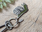 The Metal enamel keychain / purse charm | snail by ilikesara | art + goods features a detailed green snail charm and a silver-plated tag engraved with hkgifts, displayed on weathered wood with fern leaves nearby.