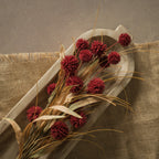 A 23" BURGUNDY POM POM BUSH by Ragon House with dried red flowers and beige leaves sits in a wooden tray on burlap fabric, displayed on a brown surface.