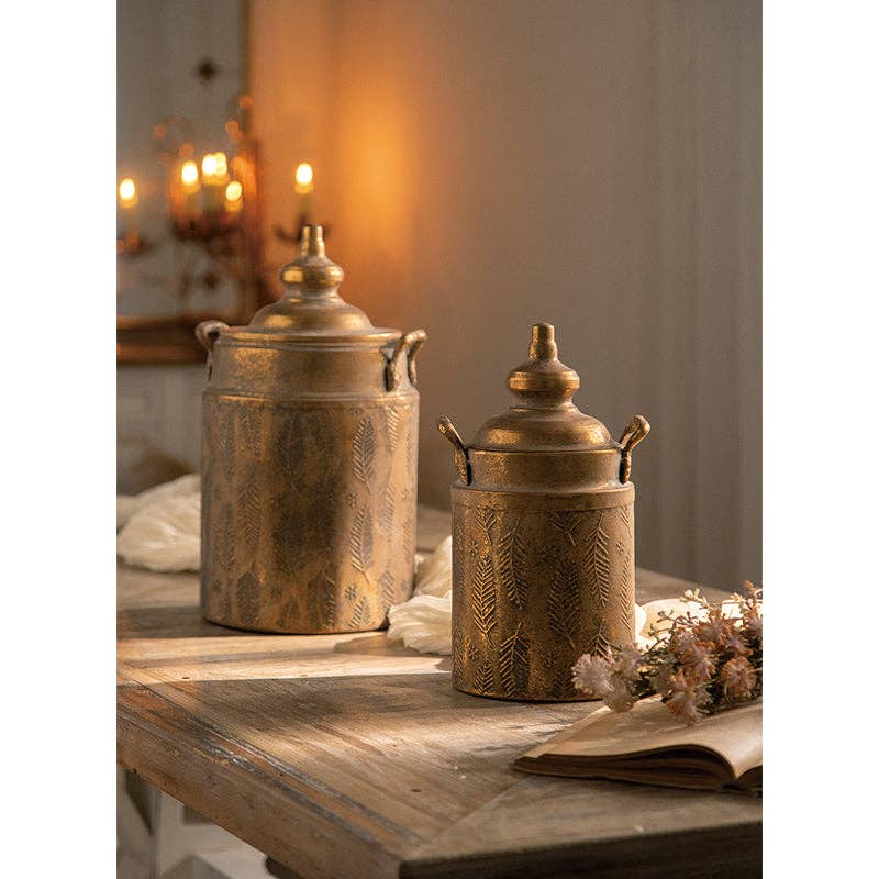 The Vintage Style Embossed Canister: Large by Vagabond Vintage sits on a rustic wooden table, surrounded by dried flowers, soft candlelight, and an open book for a cozy vintage feel.