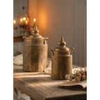 The Vagabond Vintage Vintage Style Embossed Canister: Small sits on a rustic wooden table with cozy lighting, flowers, and an open book, adding vintage charm to the scene.