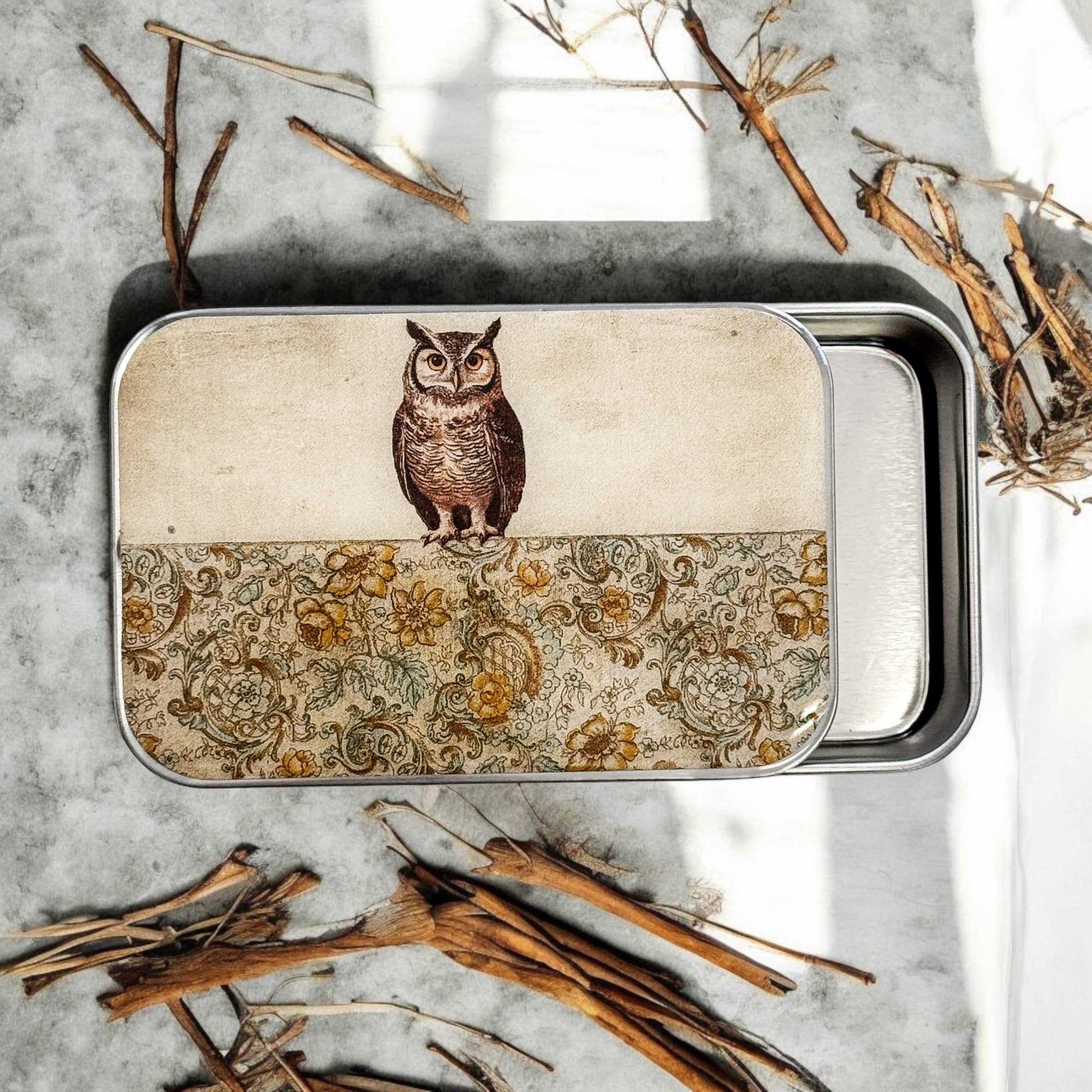The Firefly Notes Owl Notions Tin, featuring a floral-patterned lid, rests on marble with scattered twigs—an ideal decorative box to store your special keepsakes.
