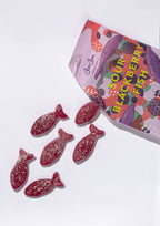 An open bag of BonBon - A Swedish Candy Co Sour Blackberry Fish - Swedish Candy 5.2oz (150g) spills six sugar-coated, vegan, fish-shaped candies onto a white background—offering a fruity twist on classic Swedish Fish.