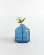 A single white flower with green leaves in the Bella Handblown Hammered Glass Bud Vase: Blush by Creative Women, set against a plain white background.