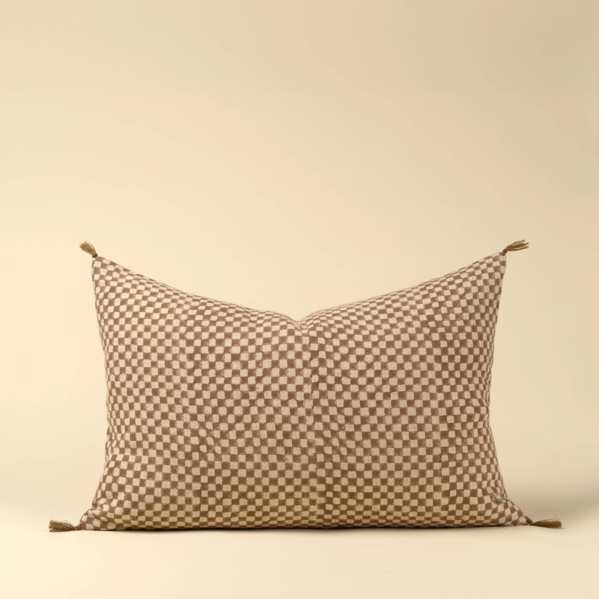 The Indaba Trading 16x24 Block Print Check Linen Pillow, Brown, features a beige and brown checkerboard pattern with small corner tassels; includes cover with filler.