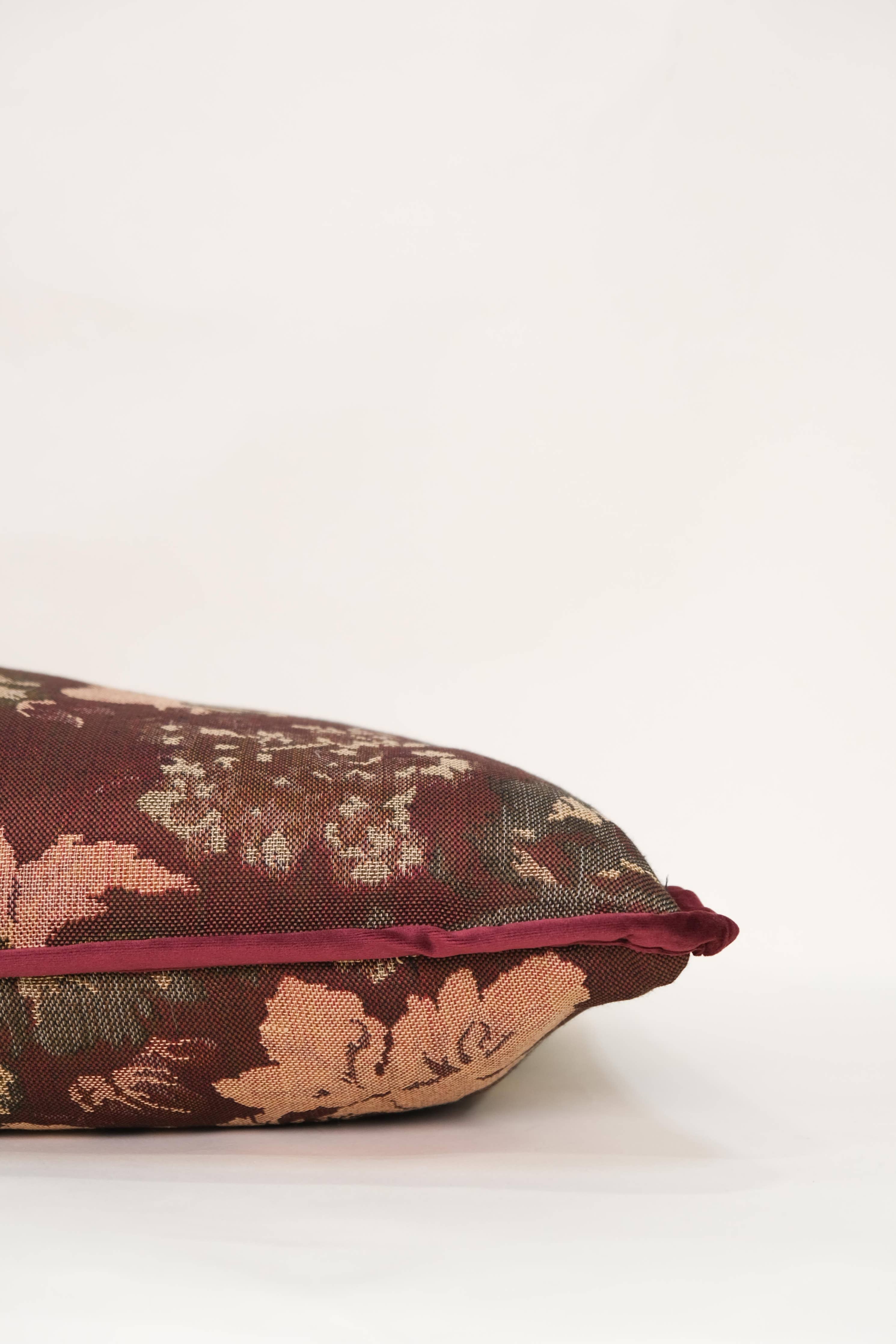 A close-up side view of the Tapestry Long Lumbar pillow by Twenty Third by Deanne, featuring a jacquard floral pattern in red, pink, and green tones against a plain white background.