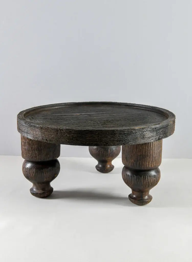The Jamali Garden 14in Wide Banjara Reclaimed Look Deep Brown/Black Rugged Wood Stand features a round silhouette with a raised edge and three sturdy, turned legs, shown against a plain, light gray background.