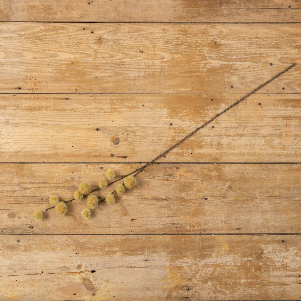 The Ragon House Faux MUSTARD GLOBE THISTLE SPRAY, featuring small, round yellow blooms, lies diagonally on a rustic wooden surface with visible knots and grain.