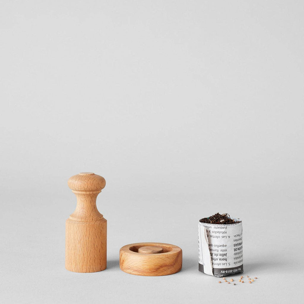 The Bloomist Gardener's Planting Set (One Size) is displayed on a plain gray background, featuring a wooden tamper, matching disc, biodegradable seedling pot with soil and seeds, plus a few scattered seeds nearby.