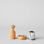 The Bloomist Gardener's Planting Set (One Size) is displayed on a plain gray background, featuring a wooden tamper, matching disc, biodegradable seedling pot with soil and seeds, plus a few scattered seeds nearby.