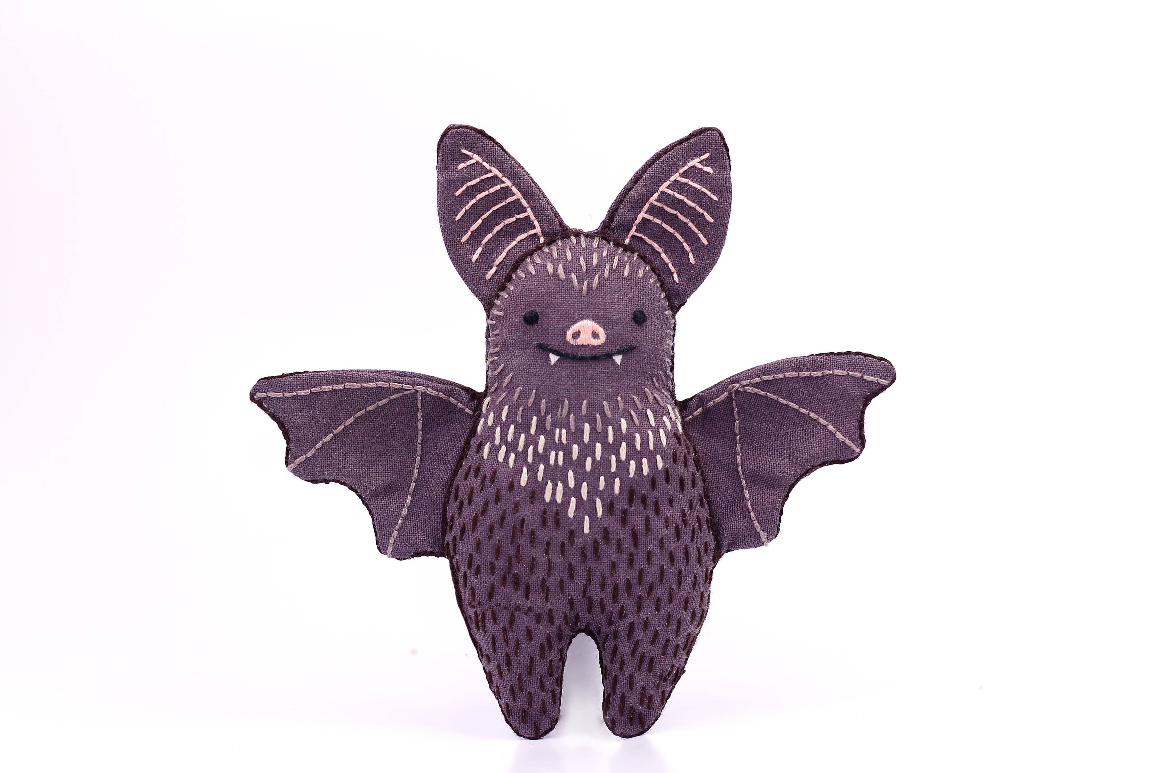 The Kiriki Press Bat - Embroidery Kit features a cute plush bat with large ears, stitched details, fangs, and outstretched wings—perfect for crafters. The finished bat stands upright against a plain white background.