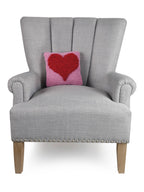 A grey chair is adorned with the Peking Handicraft Looped Heart Hook Pillow, adding a cozy, inviting touch.