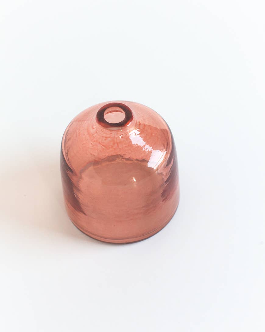 The Bella Handblown Hammered Glass Bud Vase: Blush by Creative Women features translucent, pink-tinted recycled glass and showcases its ethically hand-crafted charm on a white surface.