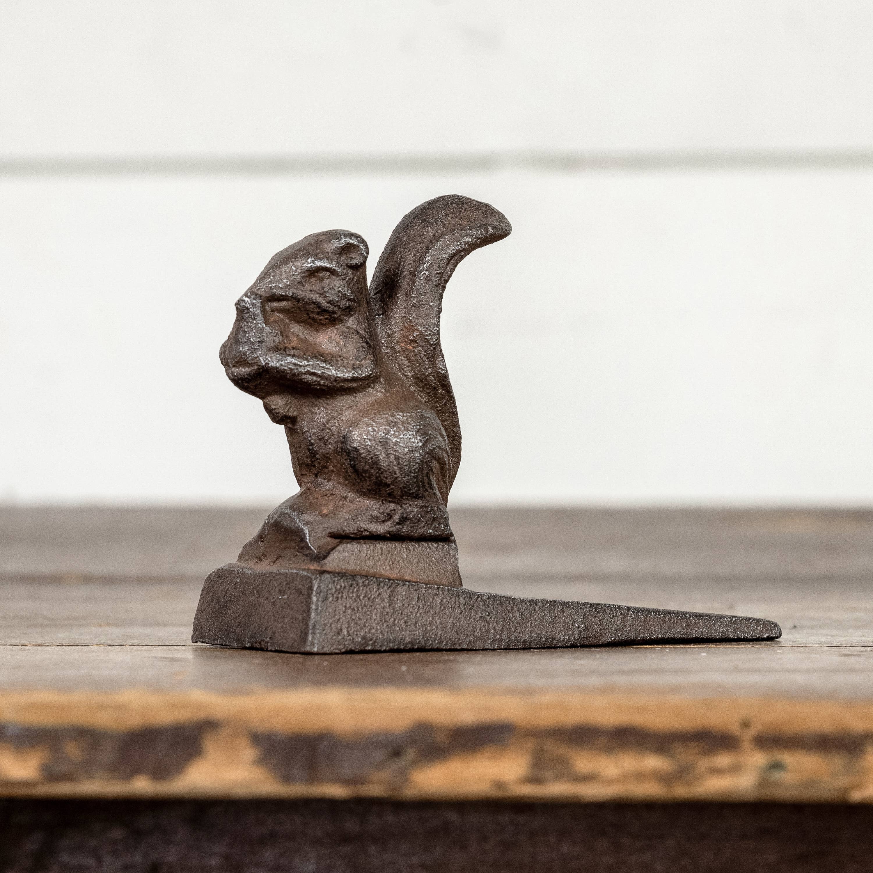 The 3.5" METAL SQUIRREL DOOR STOP by Ragon House sits upright on its wedge base, displayed on a wooden surface against a light background.