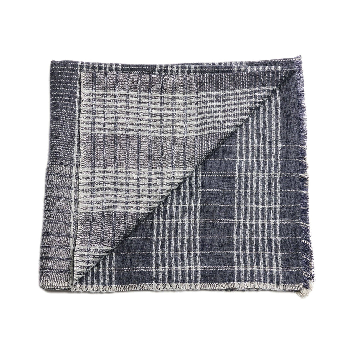 A folded Silica Rose Throw by Variously, in shades of salmon with a gray stripes pattern, is shown with one corner flipped over to reveal the reverse side. This handwoven piece features a linear striped design and frayed edges.