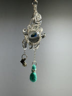 Catch • Ash Espinoza x Thyne Studio by Thyne Goods is a delicate pendant with silver wire, a clear bead, blue-green eye center, and teal felted bead, highlighting recycled sterling silver jewelry against a plain gray background.