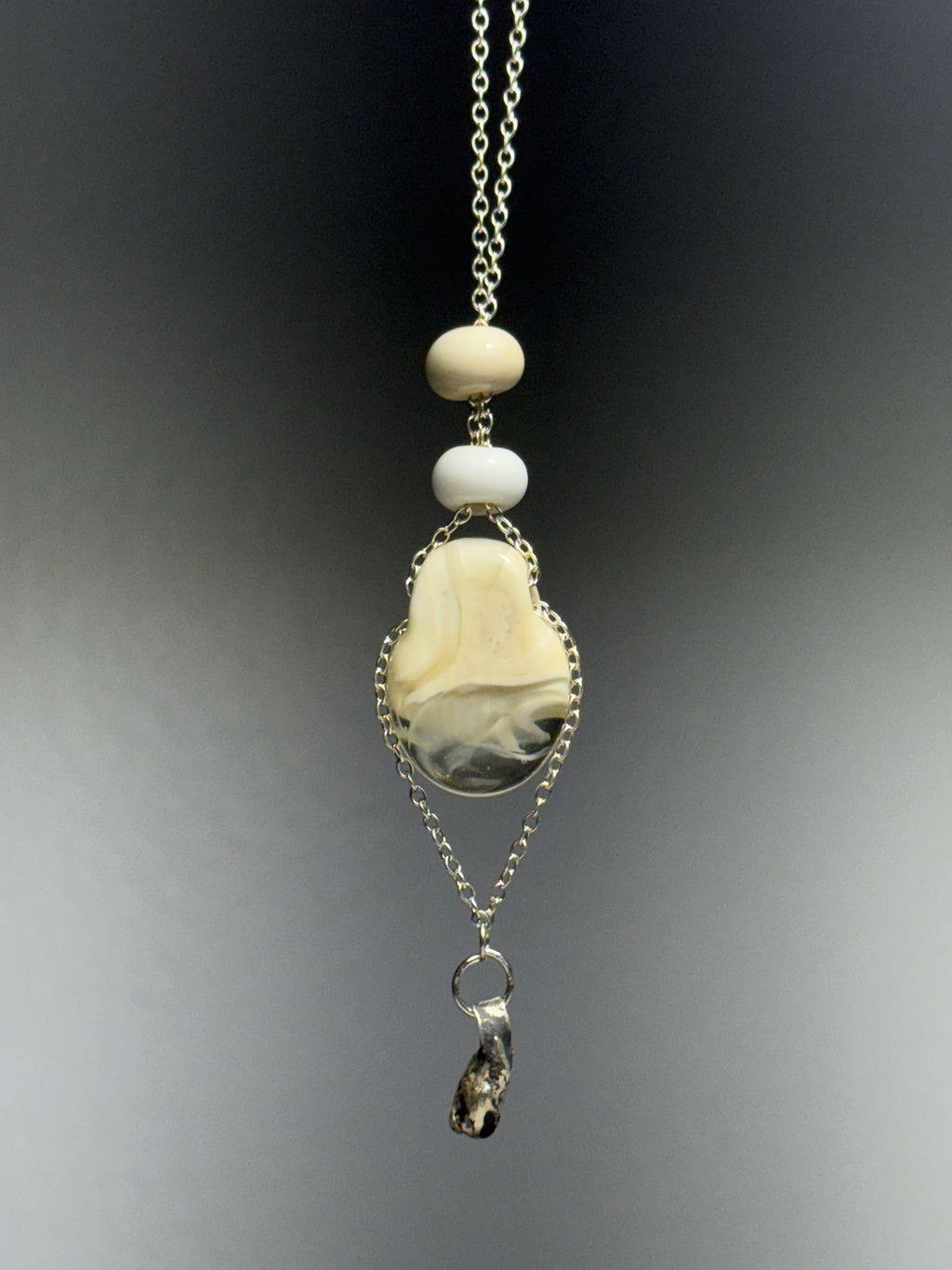 Dove by Ash Espinoza x Thyne Studio for Thyne Goods: a pendant necklace with two round white glass beads, a polished oval cream and gray stone, an irregular dark charm, all on recycled sterling silver chains over a gray gradient backdrop.