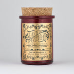The Apothecary / Love Potion / Valentine Candle by North Ave Candles is a red glass jar candle with a cork lid. Vintage label features neroli, violet, passionfruit, ginger, lemon, and thyme fragrance and a 35-hour burn time.