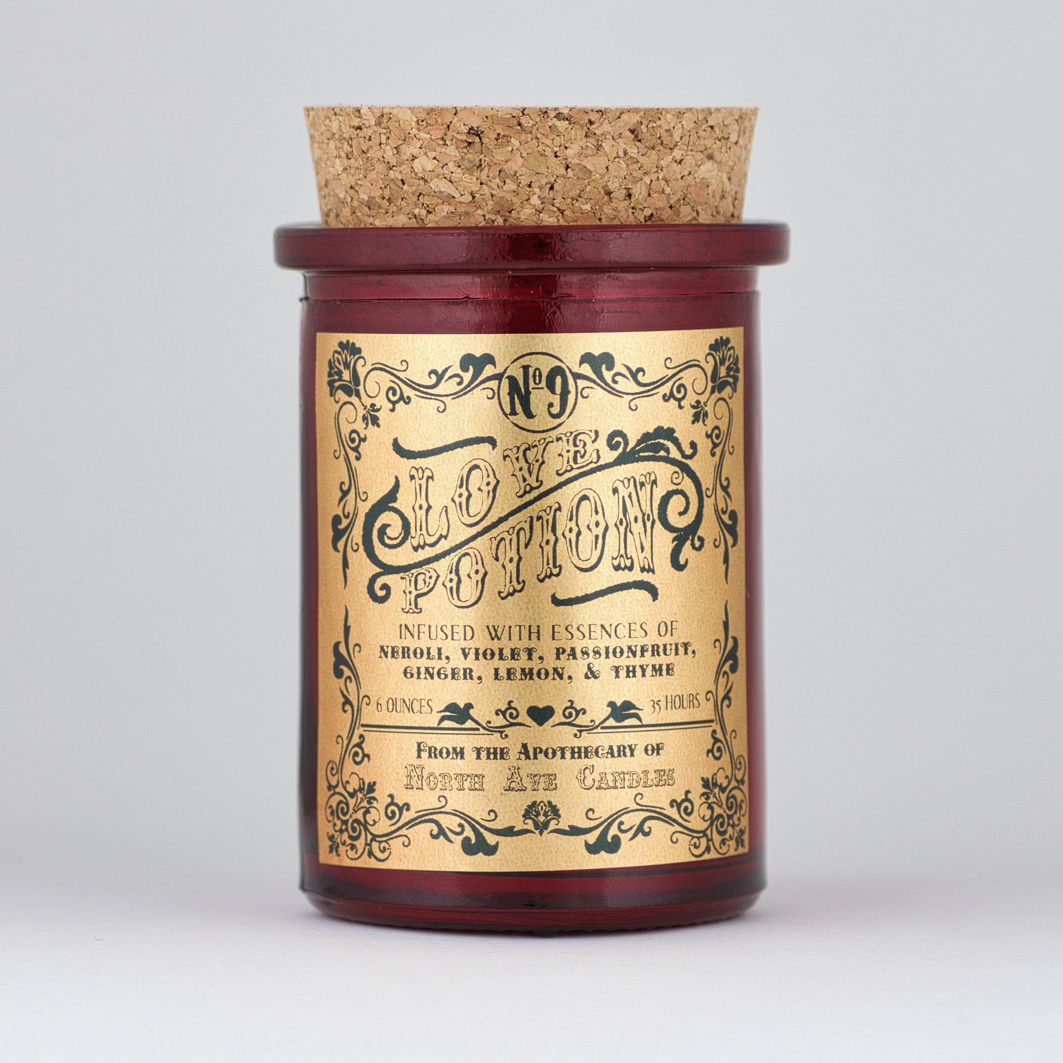 The Apothecary / Love Potion / Valentine Candle by North Ave Candles is a red glass jar candle with a cork lid. Vintage label features neroli, violet, passionfruit, ginger, lemon, and thyme fragrance and a 35-hour burn time.