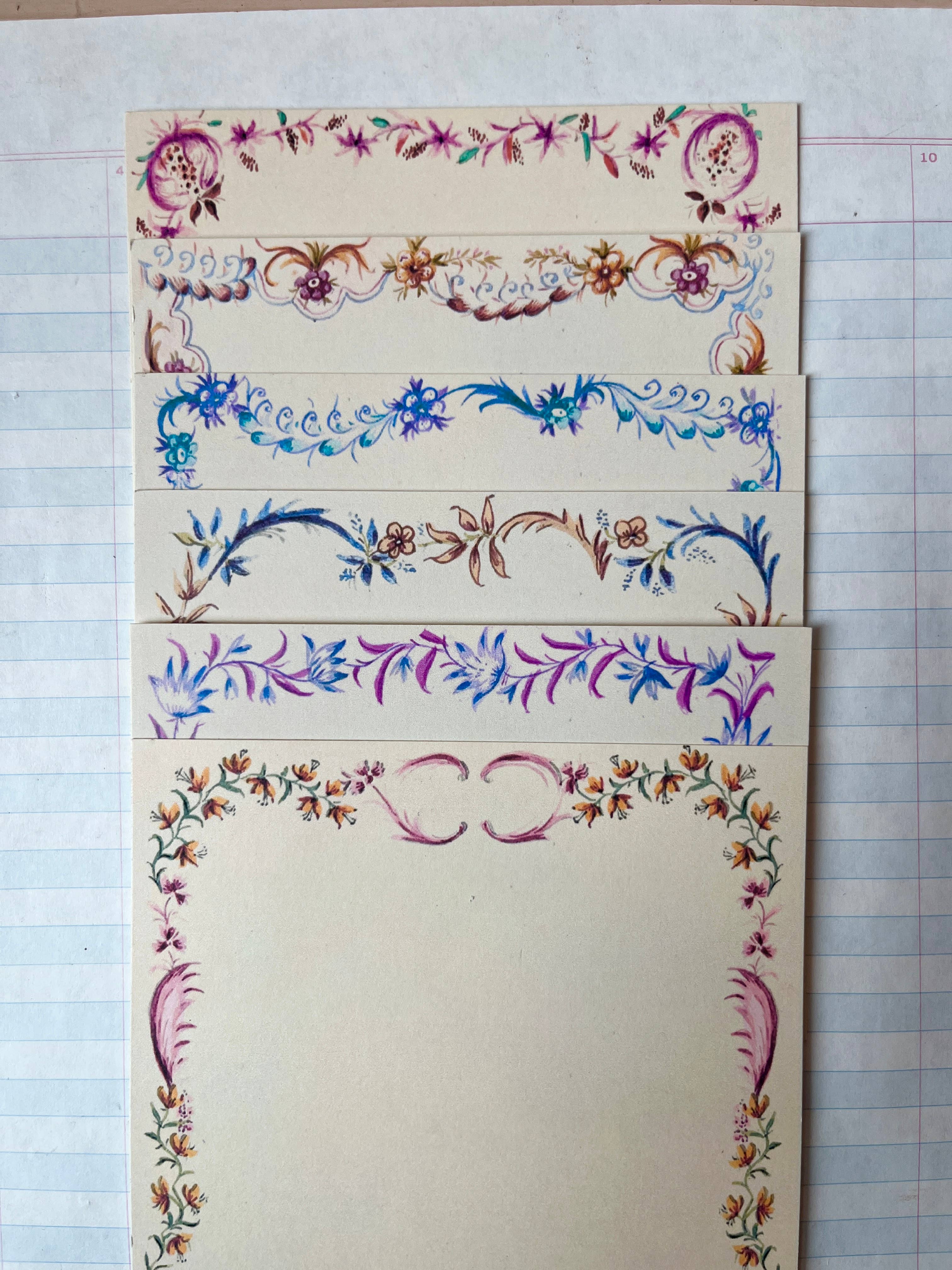 The Parcel French Menu Stationery Set II: 2 includes four creamy white cardstock cards, each with a unique, colorful hand-painted floral border in shades of purple, blue, pink, and brown on lined paper.