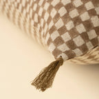 Close-up of the Indaba Trading 16x24 Block Print Check Linen Pillow in brown, featuring a beige and brown checkered design with a fabric tassel at the corner, resting on a light surface. Cover with filler included.