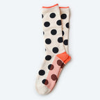 The Valley Sock by Hooray Sock Co. is a cream unisex pair with large black polka dots, orange toes and heels, plus a red and orange grid pattern on the soles, shown laid flat on a light background.
