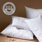 Four white Indaba Trading 24x24 Lina Linen Pillow Avocado: Cover with Filler are stacked against a neutral brown background. The upper left shows the Responsible Down Standard (RDS) Certified logo to highlight sustainable sourcing.