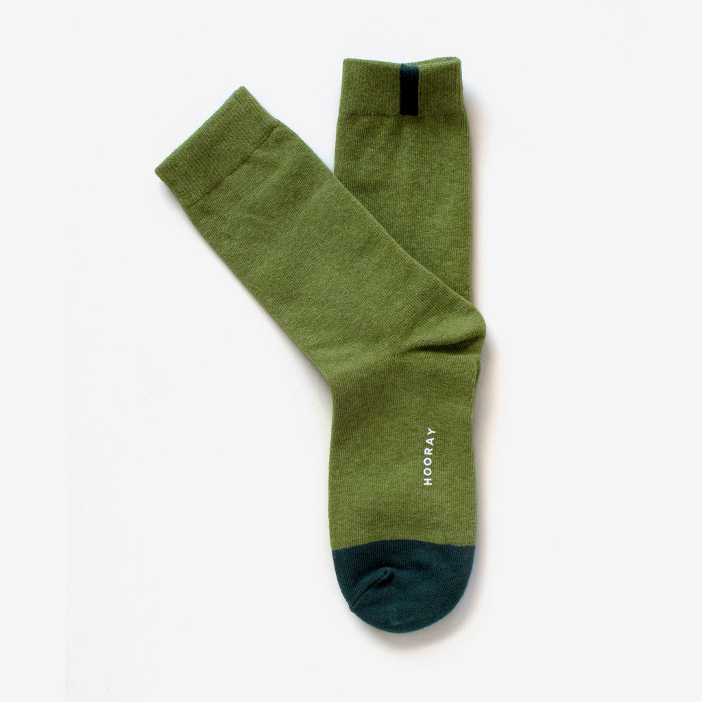 The Lafayette Moss Green Crew Socks by Hooray Sock Co. feature dark green toes, a black top stripe on one unisex sock, and “HOORAY” printed in white on the side. One size.
