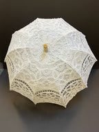 The Parasol - White by Peking Handicraft features intricate lace and a wooden handle, displayed open against a dark background—an elegant Victorian-inspired accessory for any occasion.