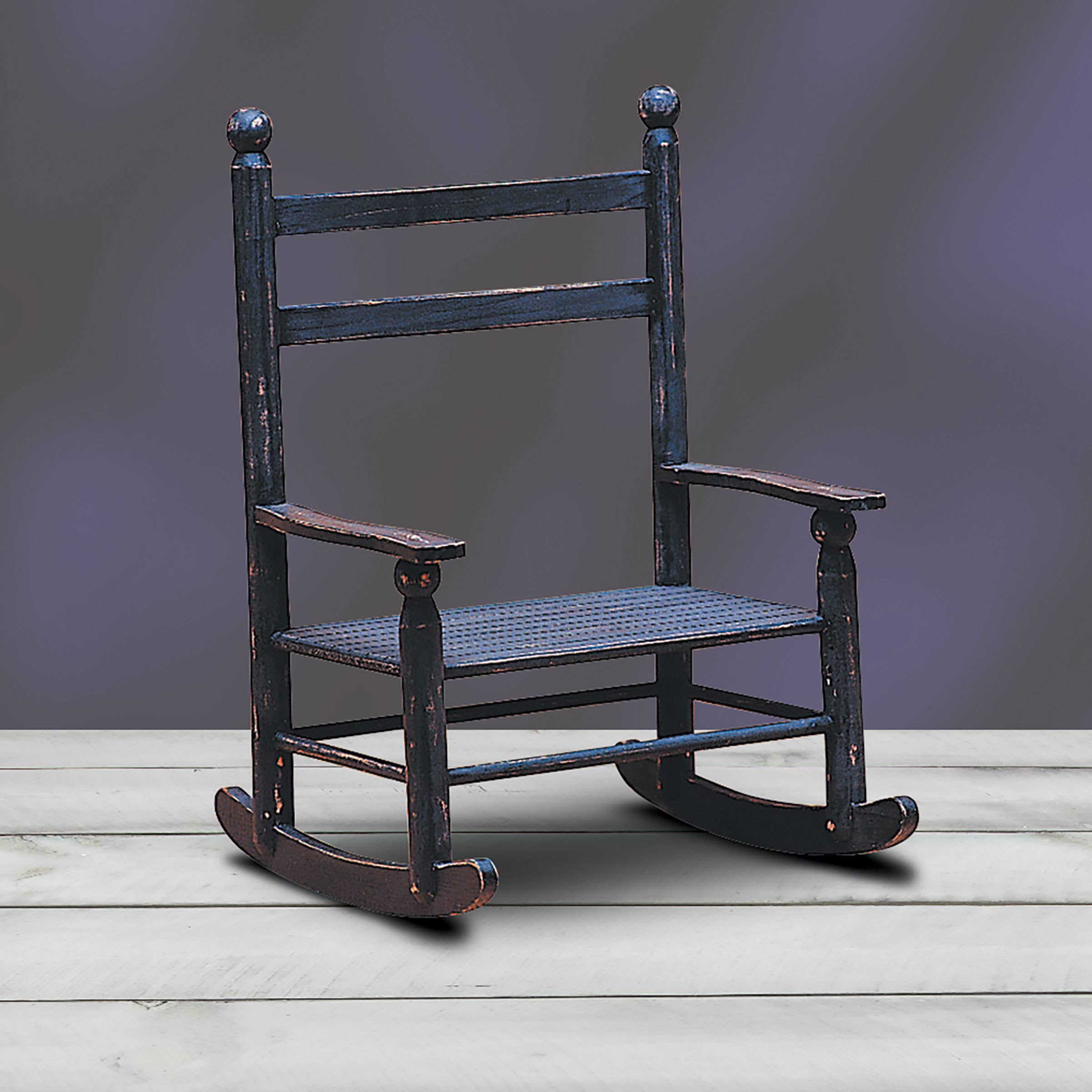 The C&F Home Mini Rustic Black Rocking Chair for Dolls features a distressed dark finish, adding vintage charm to any doll display against a light wood floor and subtle gray backdrop.