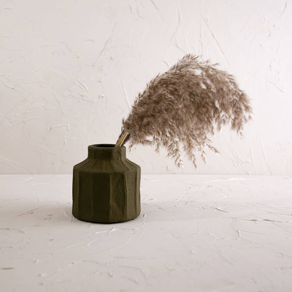 The Foreside Home & Garden Matte Green Ceramic Vase features a small, ribbed design and matte finish, perfectly displaying dried pampas grass against a light, textured backdrop.