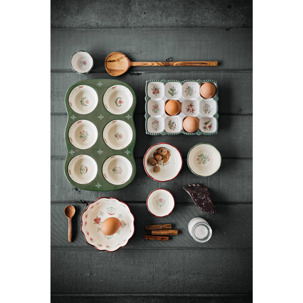 The Danica Heirloom Camellia Bowl Medium 5.75 inch, filled with eggs and nuts, is surrounded by cinnamon sticks, a wooden spoon, milk, and chocolate on a dark wooden surface.