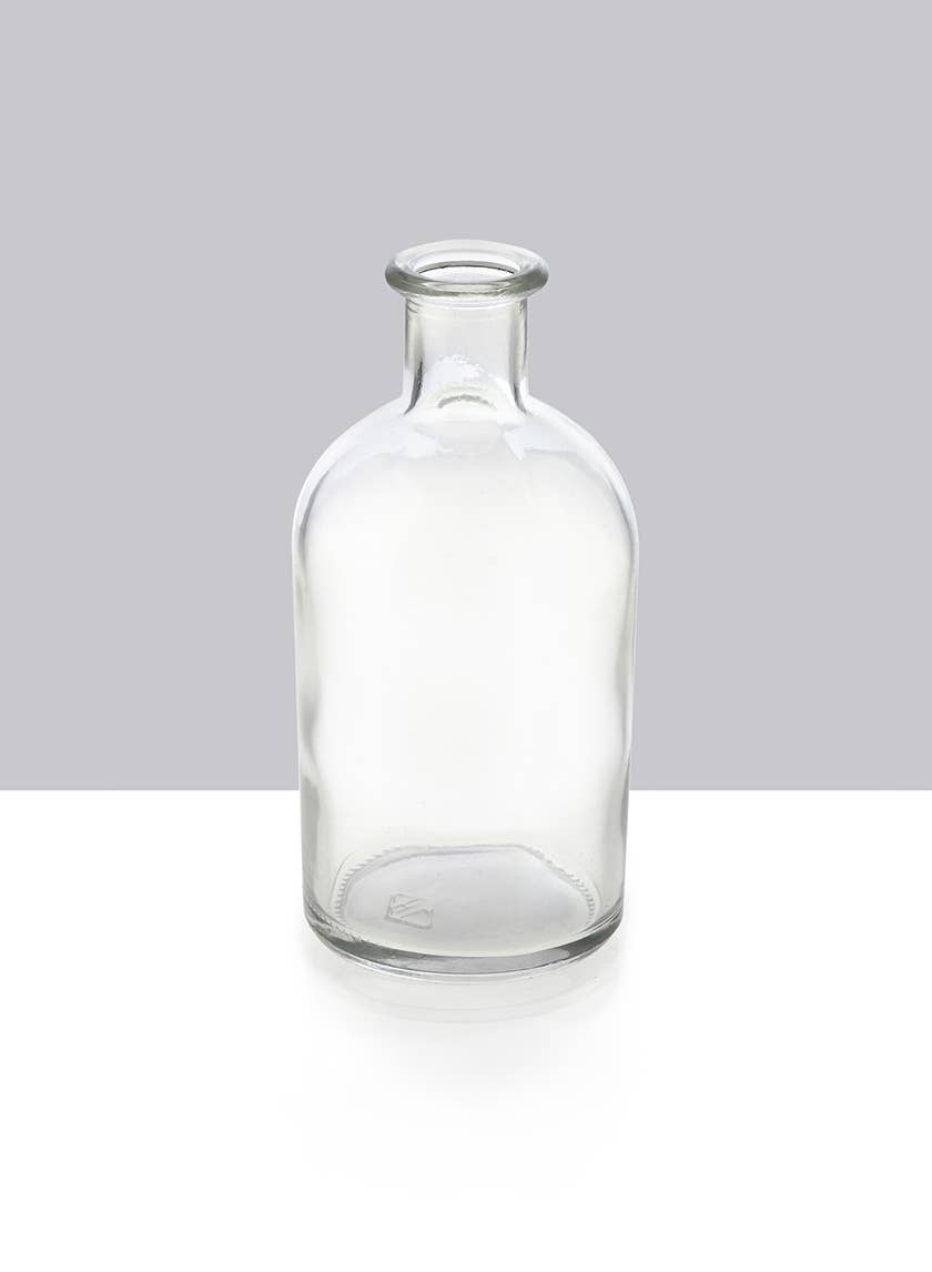 The Jamali Garden Clear Medicine Bottle Bud Vase features a narrow neck and no cap, standing upright on a white surface against a gray background—ideal for stylish home decor.