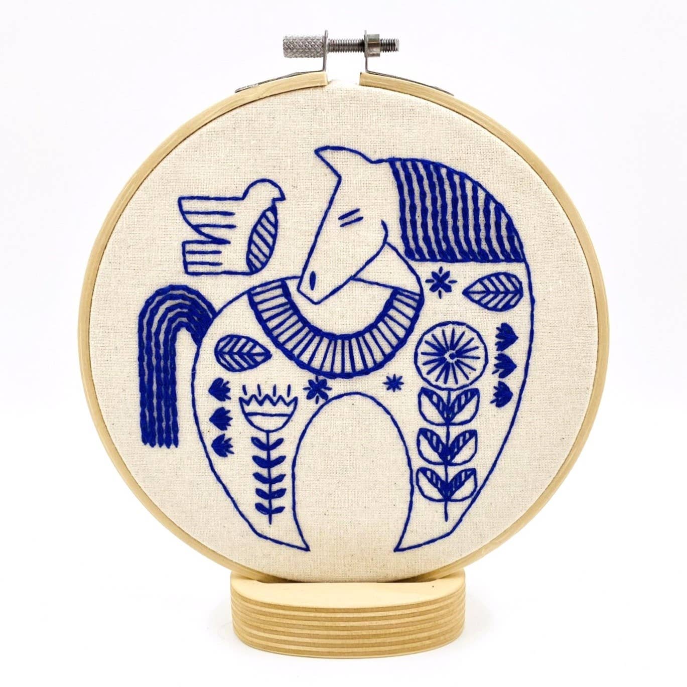 The Hygge Horse Complete Embroidery Kit by Hook, Line & Tinker features a blue stitched stylized horse with floral patterns and a bird on its back—an ideal kit for adding charm to any space.