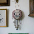 The Skippy Cotton Wonderful Wizard / Balloon Oz Wallhanging is a decorative ornament featuring a hand-stitched face, collar, thin ropes, and a fabric basket—perfect as wall art or a unique token for your space.