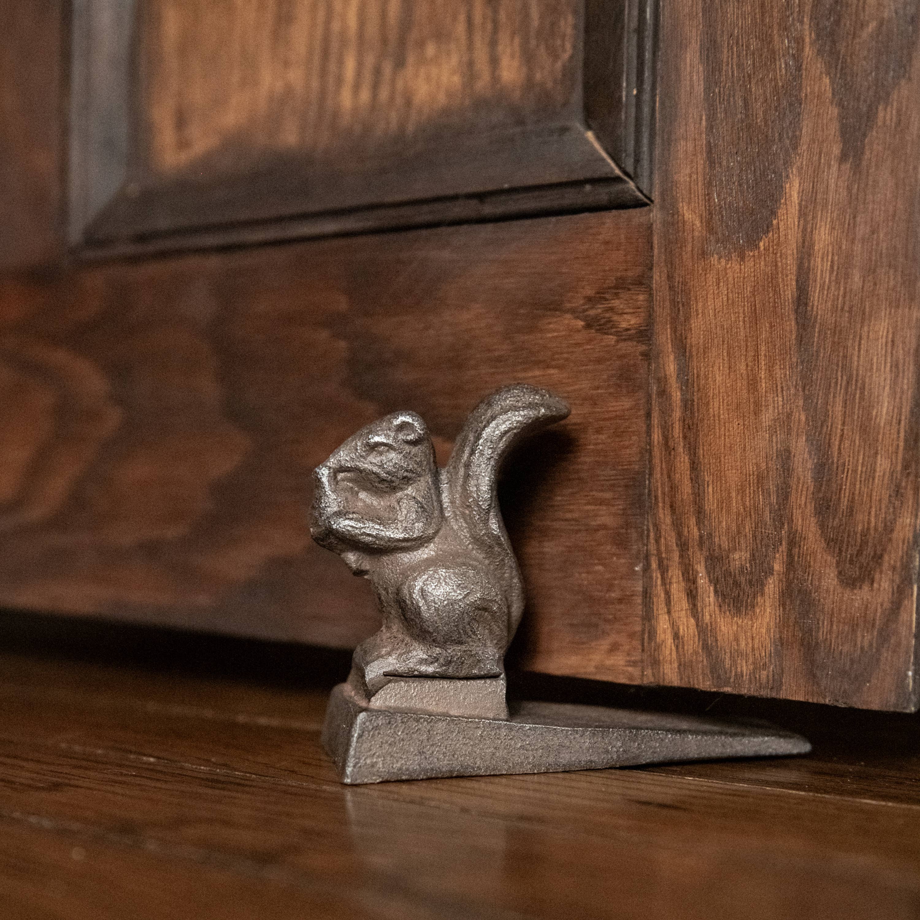 The 3.5" METAL SQUIRREL DOOR STOP by Ragon House props open a wooden door on a hardwood floor.