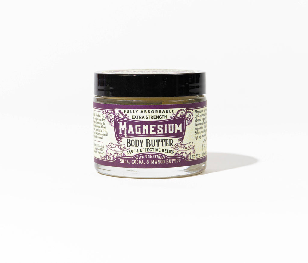 A small glass jar of Roots And Leaves Magnesium Body Butter with a black lid and purple-white label reading "extra strength," featuring shea, cocoa, and mango butter for magnesium absorption, shown on a plain white background.
