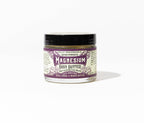 A small glass jar of Roots And Leaves Magnesium Body Butter with a black lid and purple-white label reading "extra strength," featuring shea, cocoa, and mango butter for magnesium absorption, shown on a plain white background.