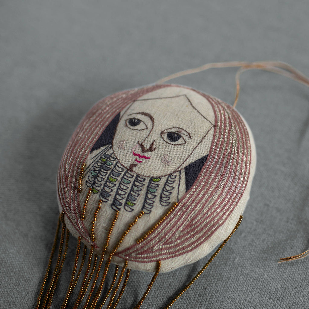 The Skippy Cotton "Wonderful Wizard / Balloon, Oz Wallhanging, Ornament, Token" features a hand-drawn face, long brown hair, stitched patterns, and gold beaded strands—perfect as Wizard of Oz textile art or a unique embroidered wall ornament.