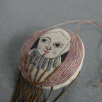 The Skippy Cotton "Wonderful Wizard / Balloon, Oz Wallhanging, Ornament, Token" features a hand-drawn face, long brown hair, stitched patterns, and gold beaded strands—perfect as Wizard of Oz textile art or a unique embroidered wall ornament.