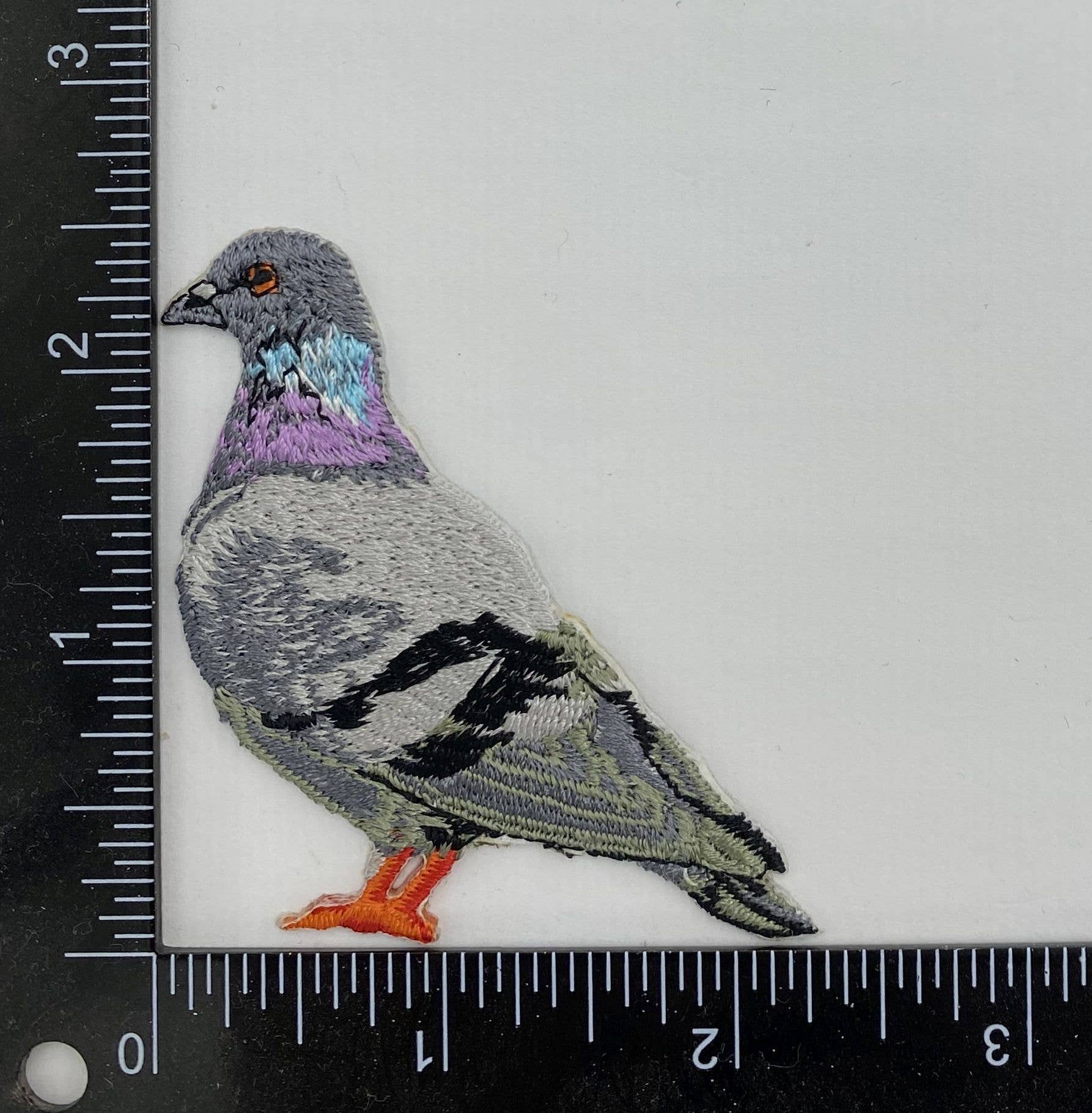 The Wholesale Applique Rock Dove Pigeon, Birds, Iron on Patch features purple, blue, gray, and black embroidery and is shown on a white background beside rulers that indicate it measures about 2 to 3 inches tall and wide.