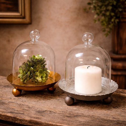 The Cloche Candle Holder with Metal Plate: Gold by Vagabond Vintage displays a green succulent and white pillar candle on a rustic wooden surface, adding charm as elegant home decor. Blurred background accents complete the look.