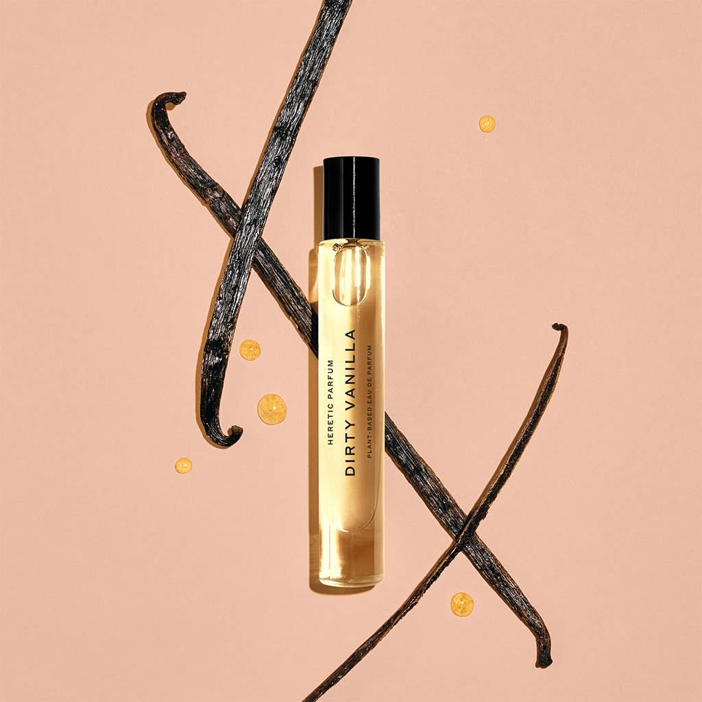 A 10ml DIRTY VANILLA ROLLERBALL by Heretic Parfum rests on a peach background, surrounded by vanilla beans, sandalwood accents, and artful drops of liquid.