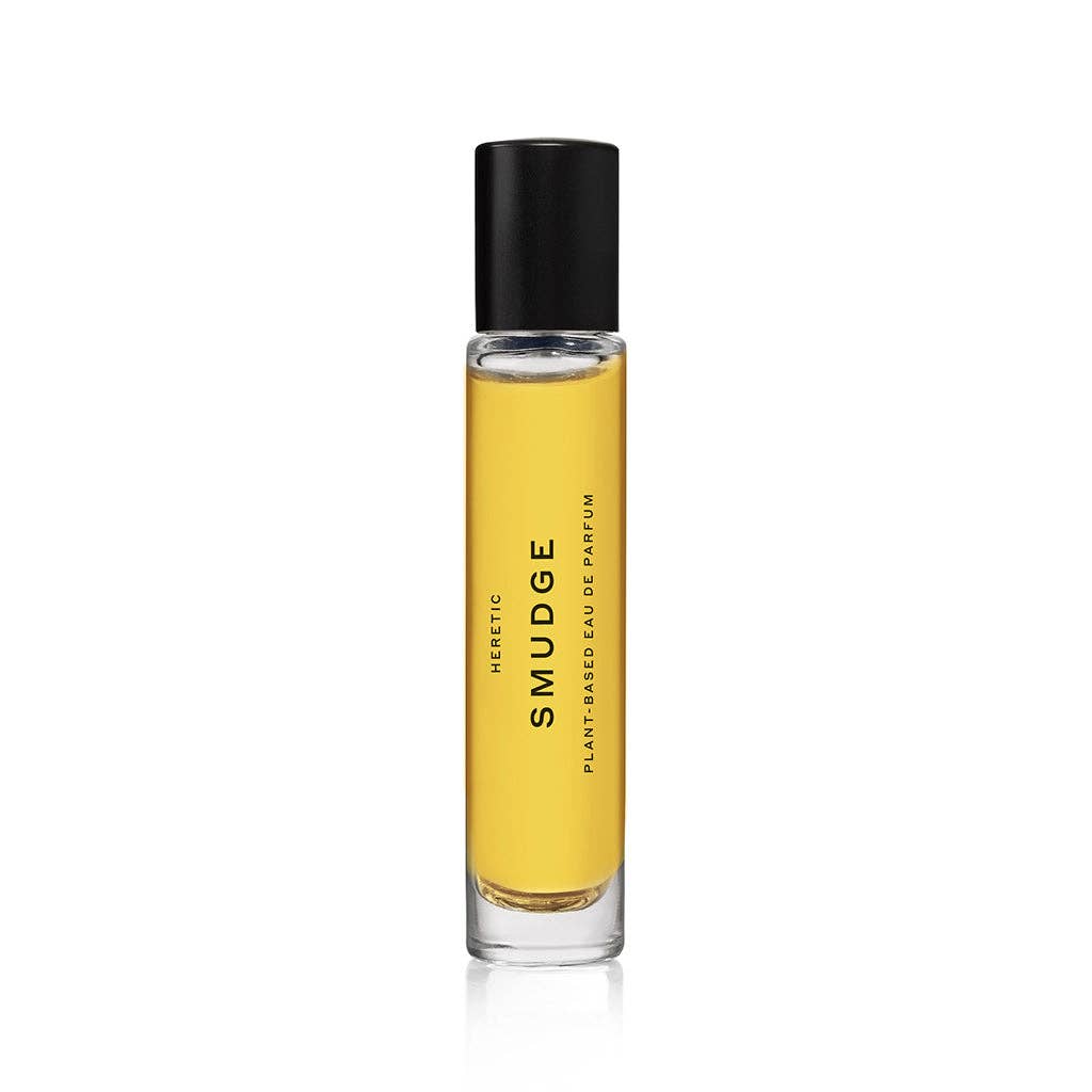 A clear glass bottle of Heretic Parfum SMUDGE: 15ML with yellow liquid and a black cap features minimalist design, suggesting notes of juniper and frankincense, displayed on a white background.
