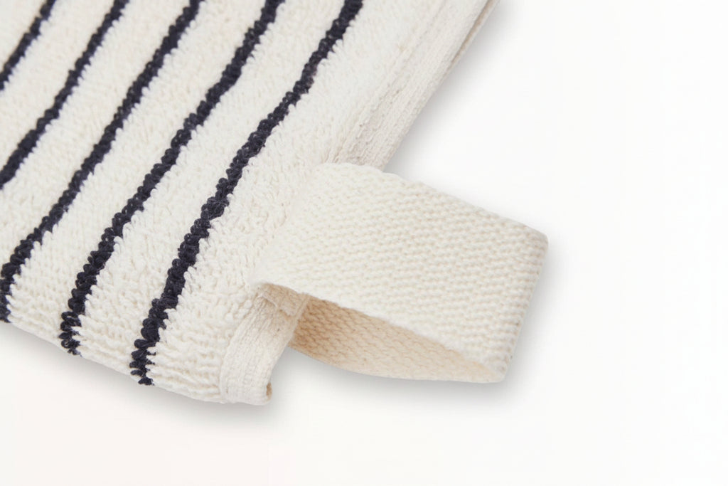 A close-up of The Loomia's Turkish Cotton Striped Terry Towel, a cream-colored bath towel with black stripes and a sewn-in loop, made from highly absorbent Turkish cotton, shown against a white background.