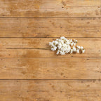 A FAUX WHITE CHERRY BLOSSOM SPRAY from Ragon House rests horizontally on a rustic wooden surface with visible grain and knots.