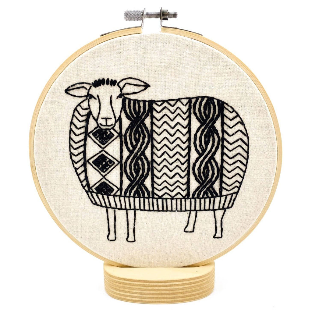 The Sweater Weather Sheep Complete Embroidery Kit by Hook, Line & Tinker features a black and white geometric sheep on a wooden base—perfect for embroidery lovers seeking a whimsical craft project.